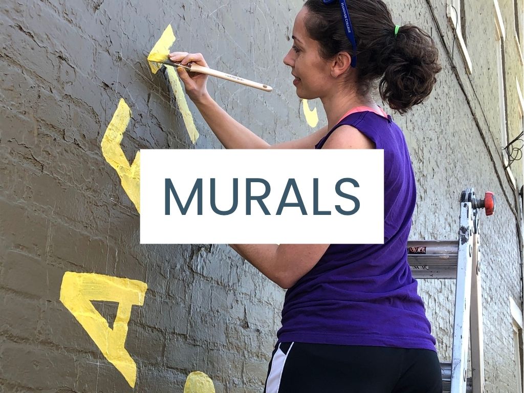 Image shows Cortlan painting letters on a brick wall with a text overlay "Murals"